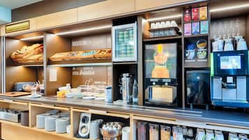 Una barra de desayuno con diversos alimentos, una máquina de café y un dispensador de fruta.