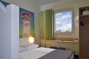 A hotel room with a bed, a nightstand, a window with curtains, a wall-mounted lamp, and a painting of a tower. - B&B Hotel Köln-frechen (Frechen)