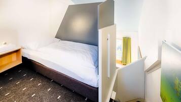 Habitación de hotel pequeña con una cama, un escritorio y una silla.