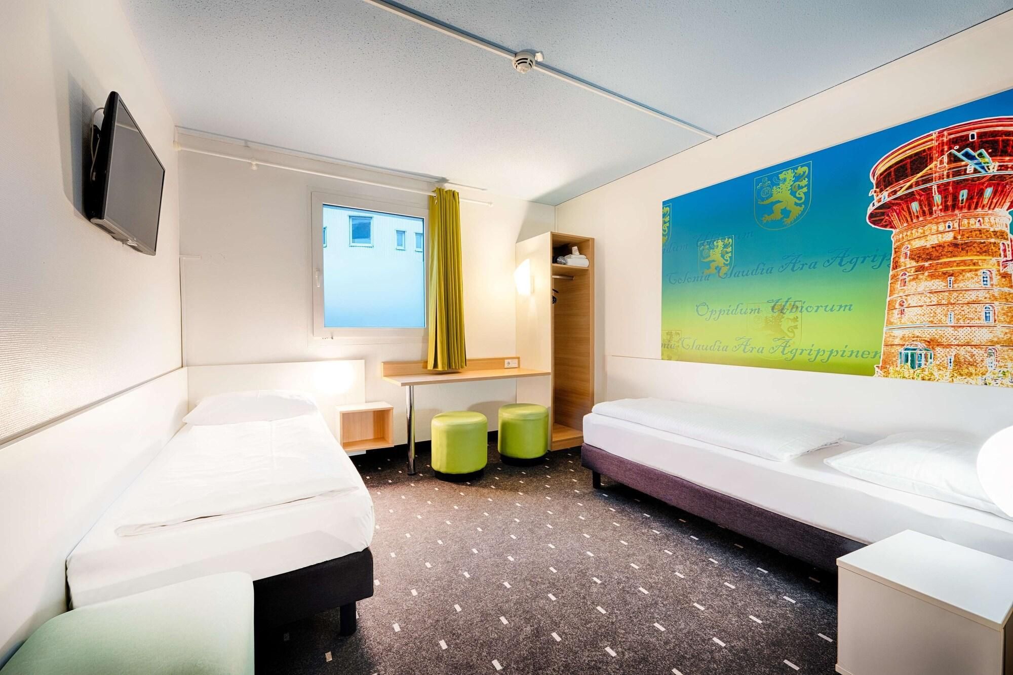 A hotel room with two beds, a desk, a chair, and a large window.