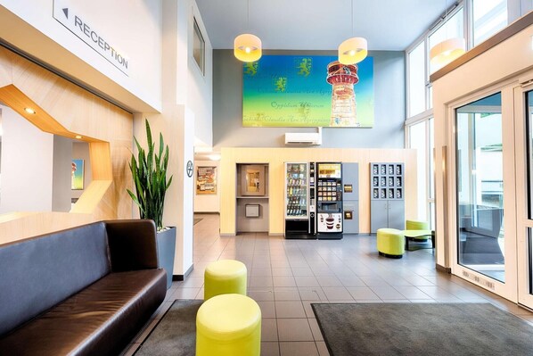 A modern reception area with a reception desk, seating, vending machines, and a large window. - B&B Hotel Köln-frechen (Frechen)
