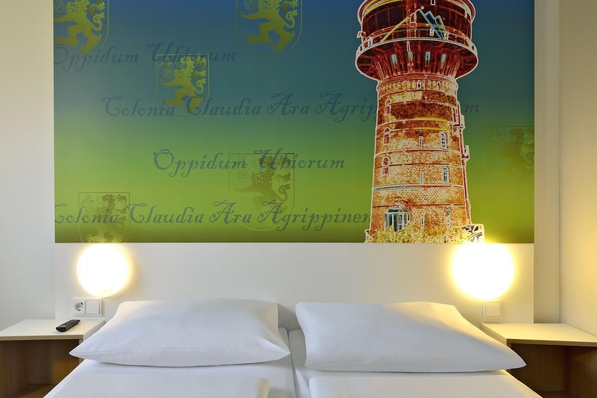 Une chambre d’hôtel avec une grande fresque murale représentant un phare, deux lits blancs et des lampes de chevet.