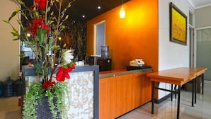 A reception area with a wooden reception desk, a large vase with red flowers, and a water dispenser. - Chiaro Hotel Syariah (Sidoarjo)