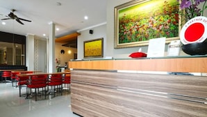 A hotel reception area with a wooden reception desk, red chairs, and a large floral painting above the desk. - Chiaro Hotel Syariah (Sidoarjo)