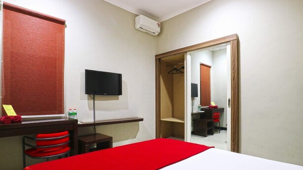 A hotel room with a bed, a desk with a chair, a television, a wardrobe, and a mirror. - Chiaro Hotel Syariah (Sidoarjo)