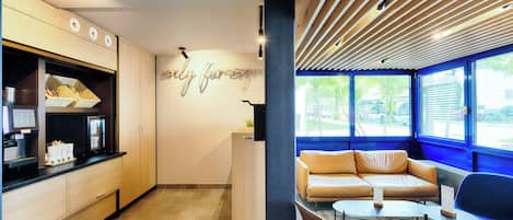 Una cocina moderna con cafetera integrada, una zona de estar con sofá y sillones, y una pared con un letrero decorativo.