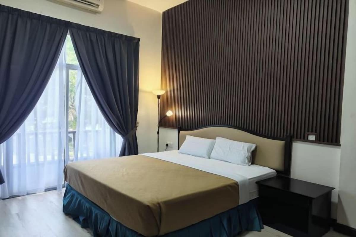 A hotel room with a bed, a nightstand, a lamp, and a view through a window with curtains.