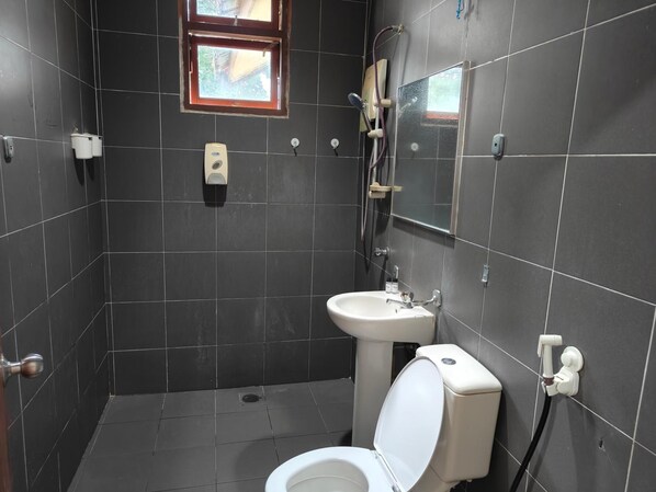 A small, dark-tiled bathroom with a toilet, sink, and shower. - Terengganu Equestrian Resort (Kuala Terengganu)