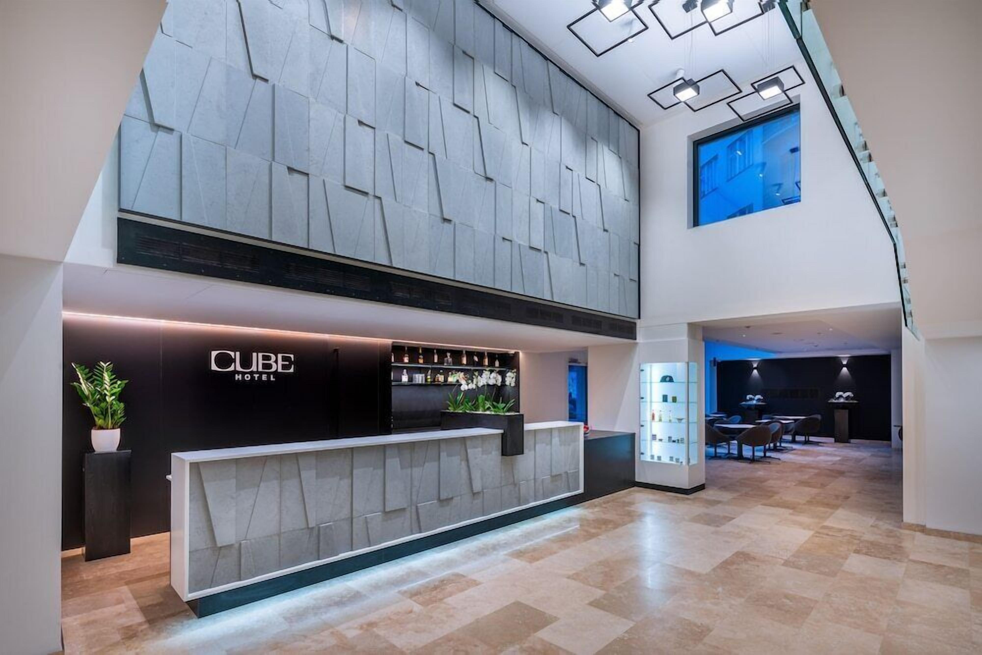 A hotel reception area with a modern design, featuring a reception desk, a bar area, and a seating space.