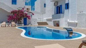 Une piscine à bords incurvés, des bâtiments blancs rehaussés d’éléments bleus et un escalier menant à un balcon.