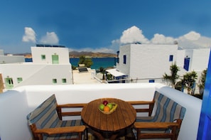 A terrace with white buildings, a wooden table with fruit, and blue and white furniture.