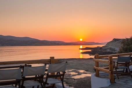 A sunset view from a beachside seating area with chairs and a wooden railing.
