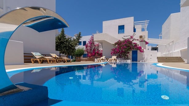 A clear blue pool surrounded by white buildings, with lounge chairs and pink bougainvillea plants. - Apollon Rooms (Milos)