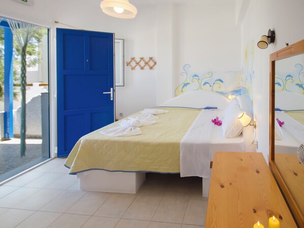 A bedroom with a bed, a wooden dresser, a blue door, and a view of the outside. - Apollon Rooms (Milos)