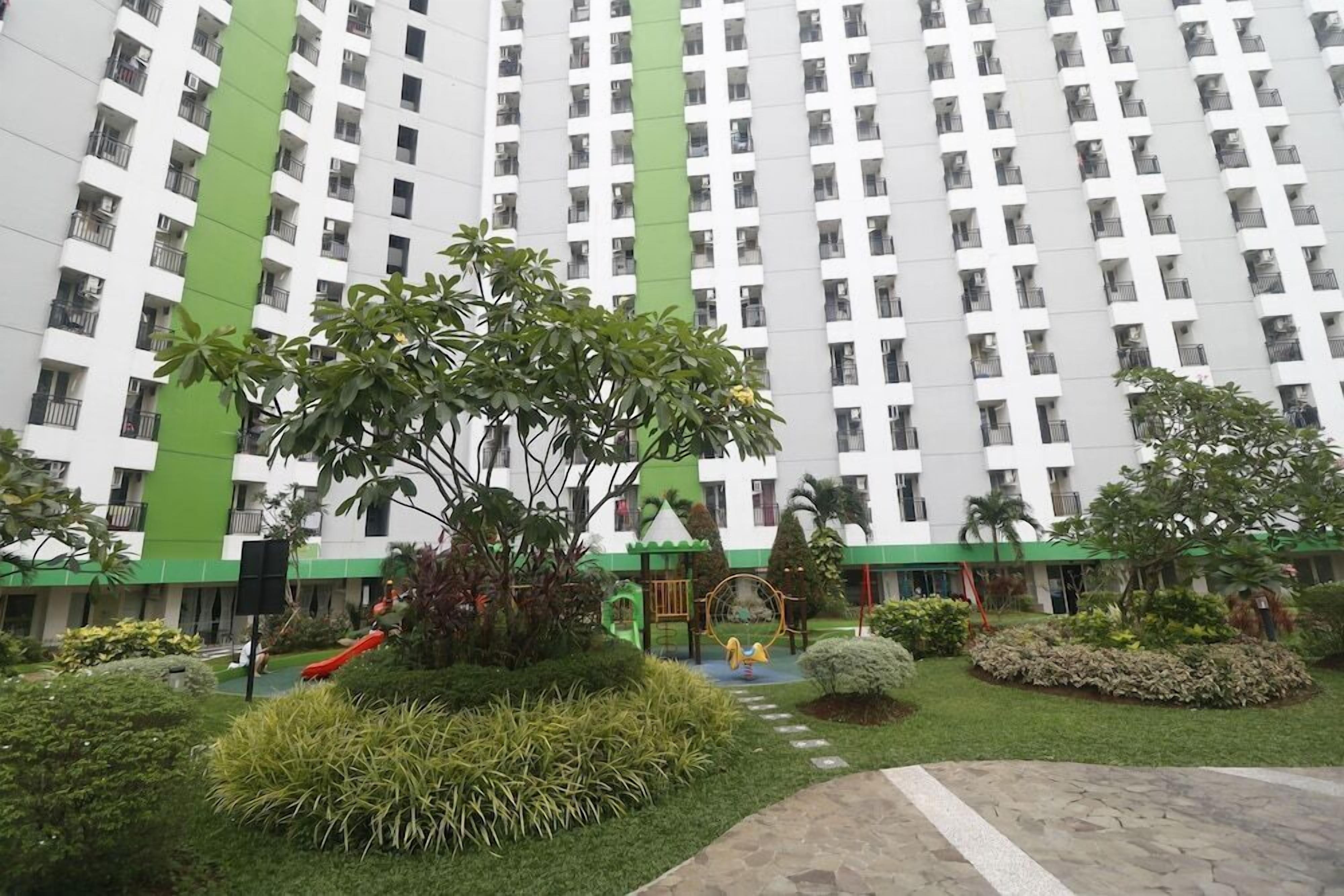 A high-rise building with a green and white facade, surrounded by well-maintained gardens and a playground.