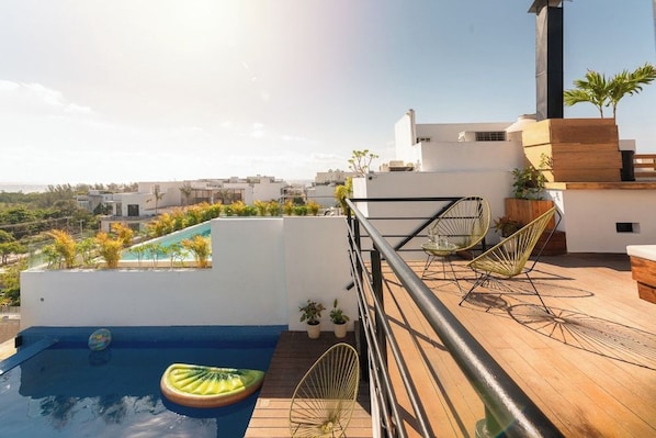 Un área de piscina en la azotea con vista a la ciudad, una terraza de madera y dos sillas de alambre verdes.