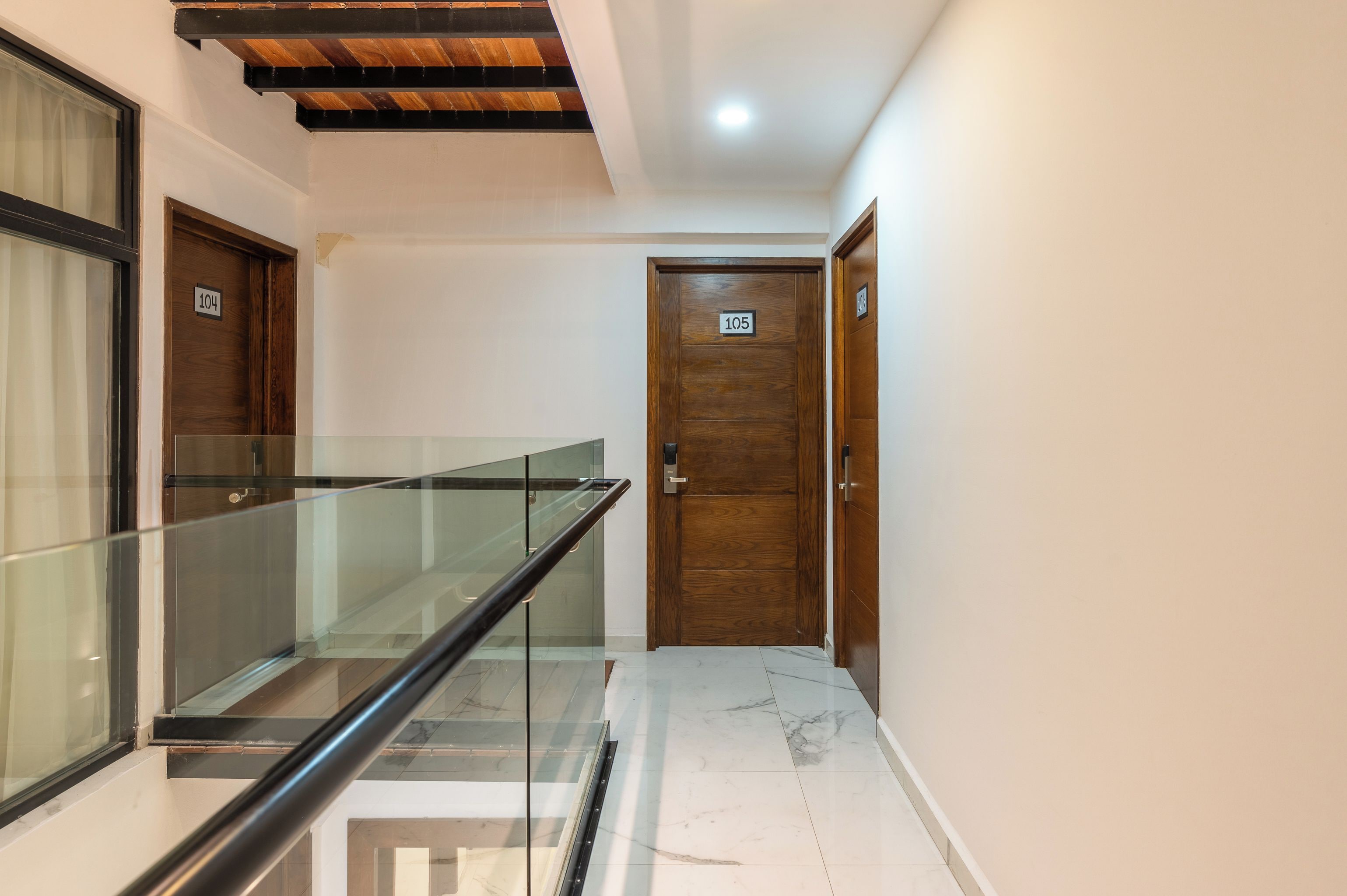 A hallway with a glass railing, wooden doors numbered 104 and 105, and a tiled floor.