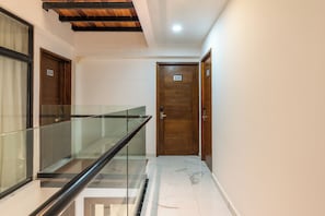 Un pasillo con barandilla de vidrio, puertas de madera con los números 104 y 105, y piso de baldosas.