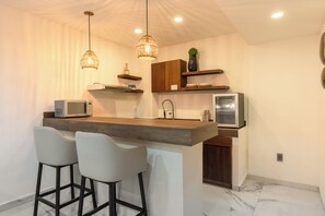 A modern kitchen with a wooden island, two bar stools, a microwave, a refrigerator, and pendant lighting. - Marvic Hotel (Playa del Carmen)