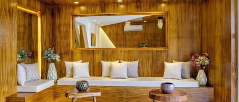 A modern interior with a wooden panel wall, a sofa with cushions, a side table, a round table, and a mirror.
