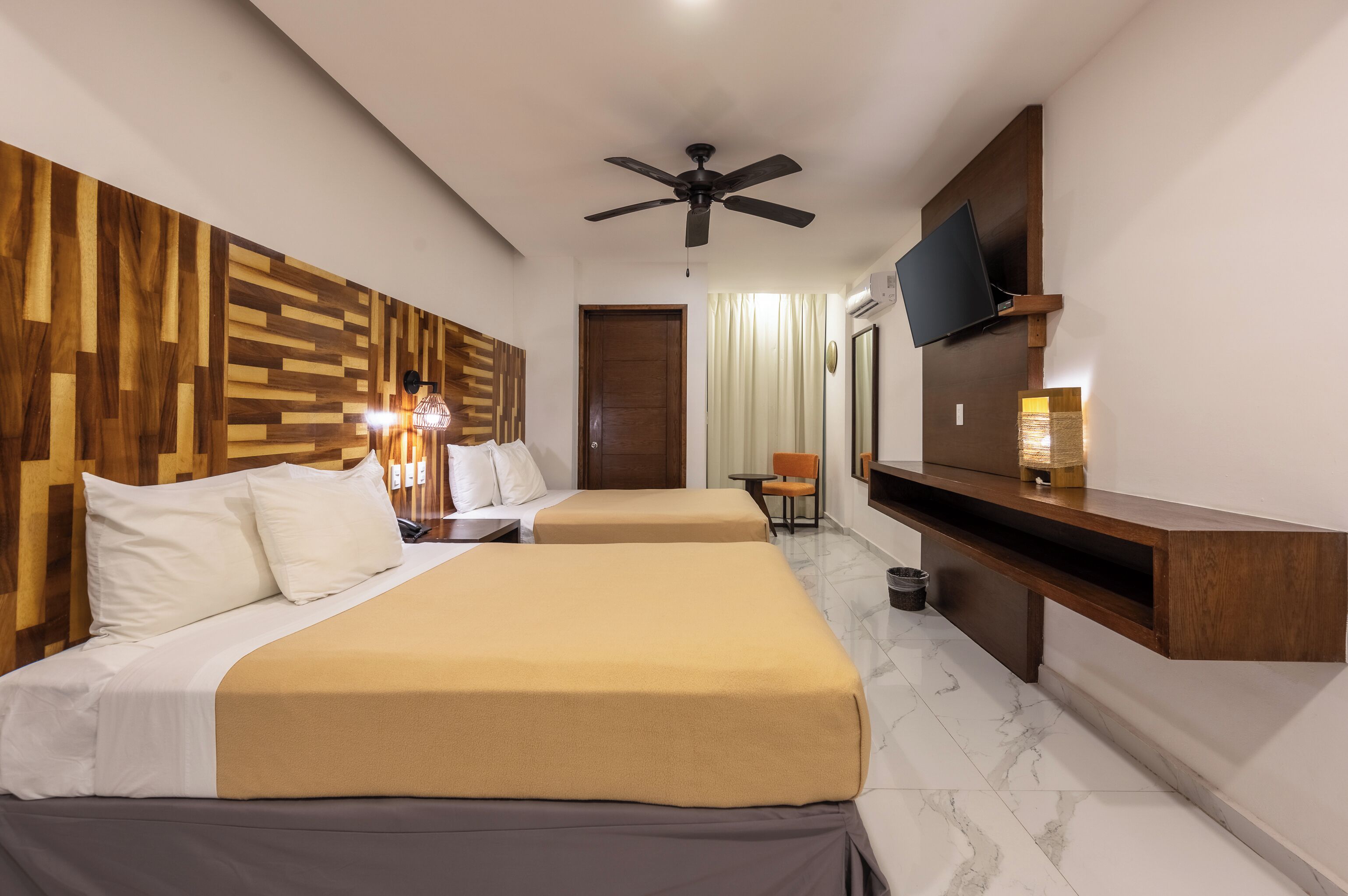 A hotel room with two beds, a ceiling fan, a TV, a desk, and a chair.
