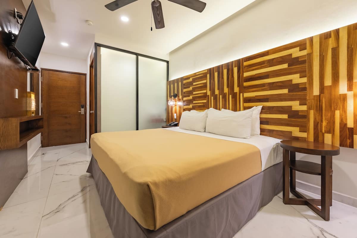 Une chambre à coucher comprenant un lit, une tête de lit en bois, une table de chevet, un téléviseur posé sur un meuble et une armoire.