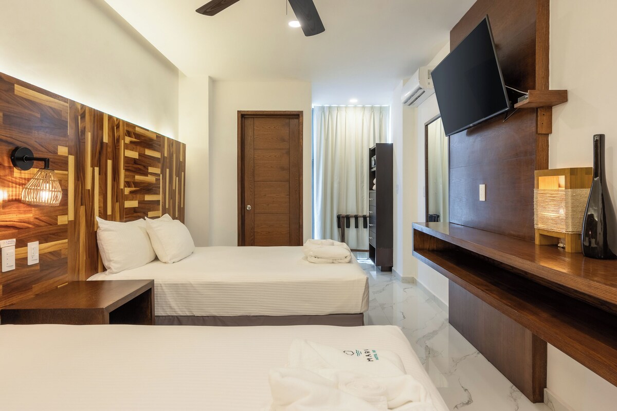 A hotel room with two beds, a TV mounted on the wall, a wooden headboard, and a fireplace.