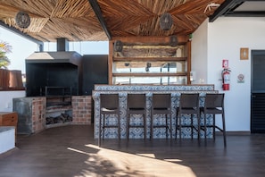 Un área de bar al aire libre con chimenea de ladrillo, sillas de mimbre y un reverso de azulejos decorativos.