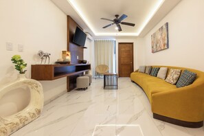 A modern living room with a curved sofa, a ceiling fan, a mounted TV, and a marble floor. - Marvic Hotel (Playa del Carmen)
