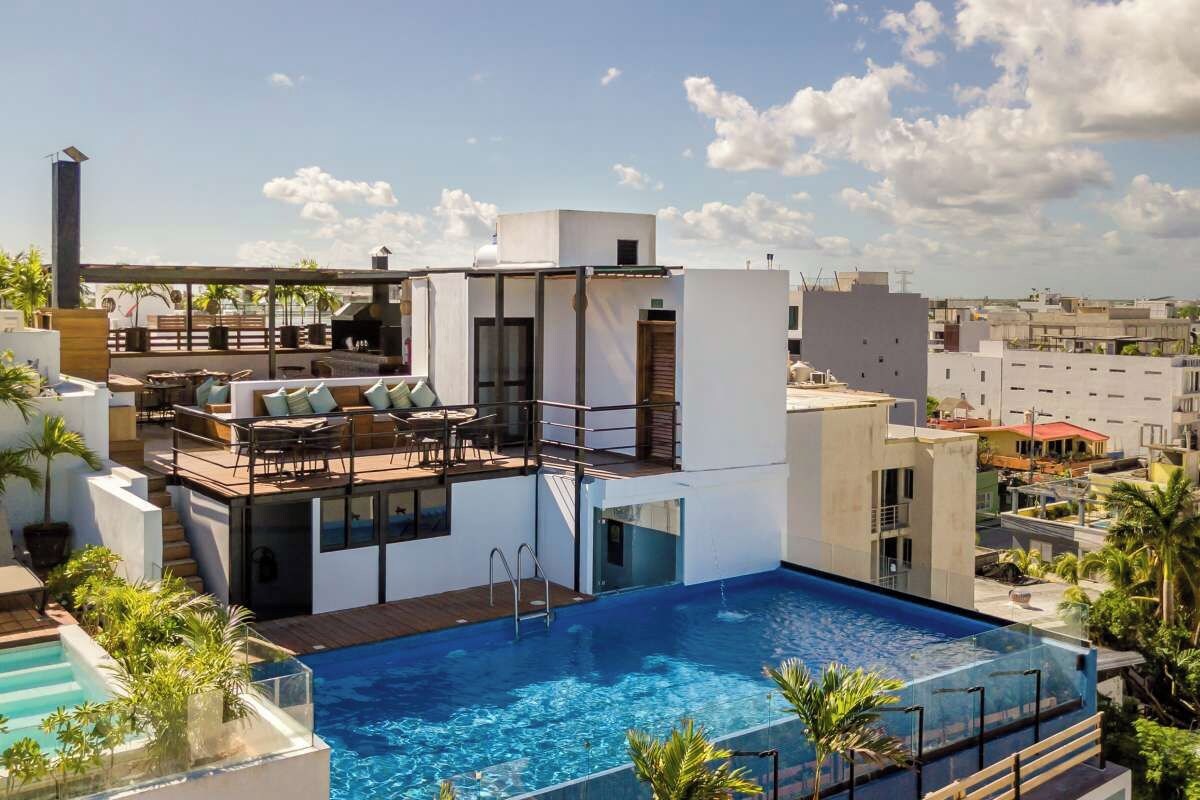 A rooftop pool with a modern outdoor seating area, a clear view of the cityscape, and a multi-level structure with glass railings.
