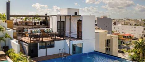 A rooftop pool with a modern outdoor seating area, a clear view of the cityscape, and a multi-level structure with glass railings.