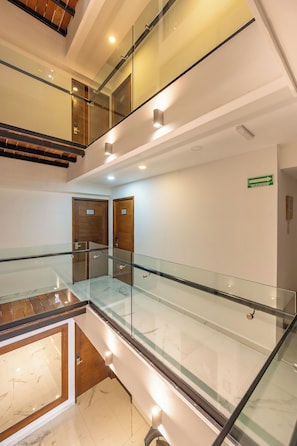 A modern hotel interior with a glass railing, marble flooring, wooden doors, and a staircase. - Marvic Hotel (Playa del Carmen)