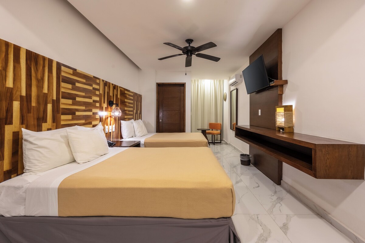 A hotel room with two beds, a ceiling fan, a TV, a desk, and a chair.
