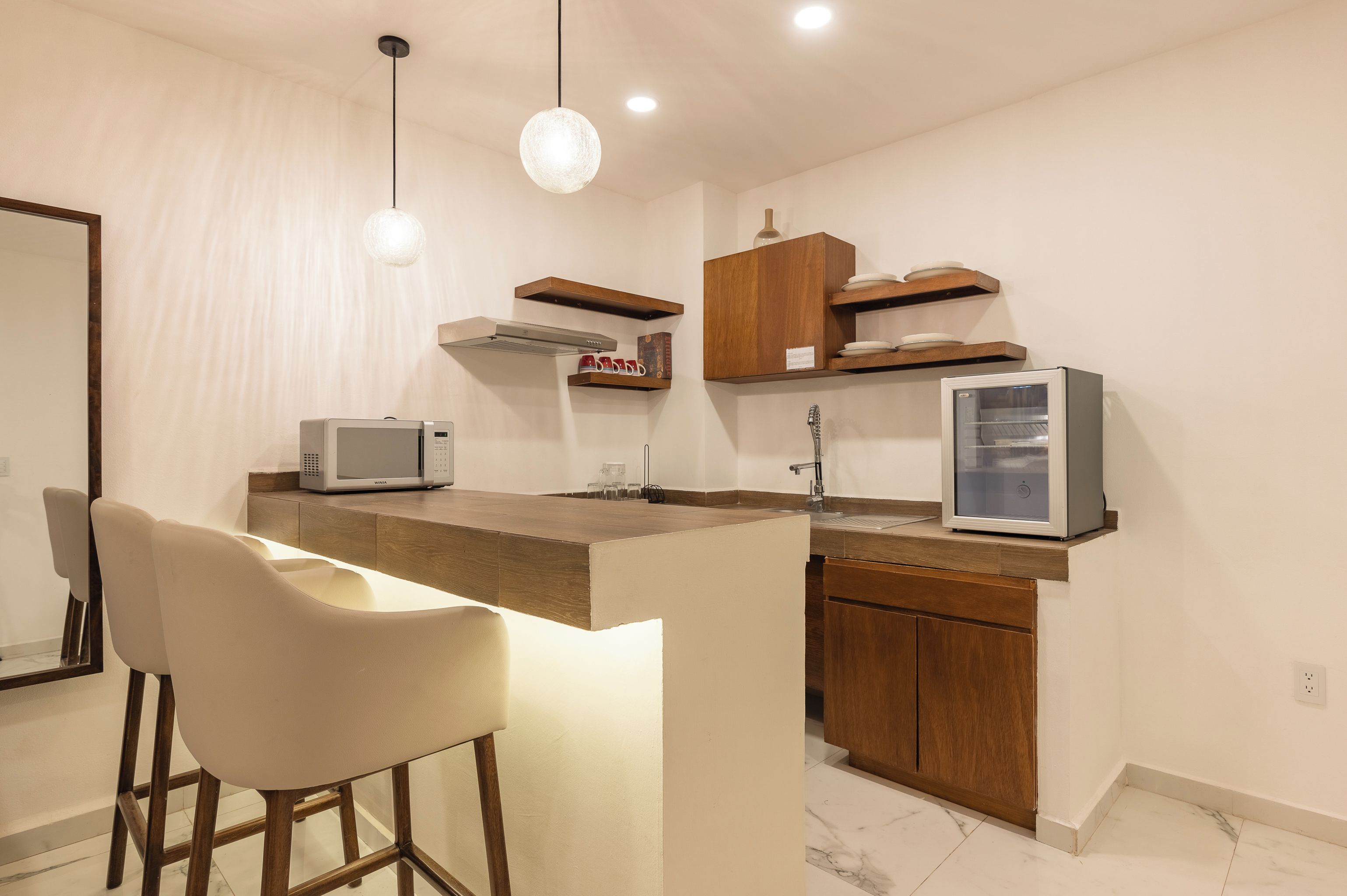 Une cuisine moderne avec un plan de travail en bois, des tabourets de bar blancs, un four à micro-ondes, un réfrigérateur et des placards en bois.