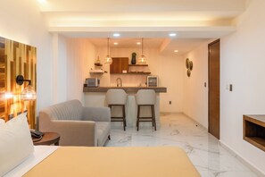 A modern hotel room with a bed, a sofa, two bar stools, a small kitchen area, and a wooden accent wall. - Marvic Hotel (Playa del Carmen)
