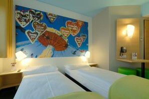 Ein Hotelzimmer mit zwei Betten, einer großen Wandmalerei mit Herzmotiv, Nachttischlampen, einem Telefon am Nachttisch und einem grünen Hocker.
