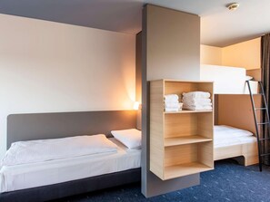 Ein modernes Hotelzimmer mit Etagenbett, einer Holztrennwand mit gefalteten Handtüchern, einer Leiter und einer Wandleuchte.
