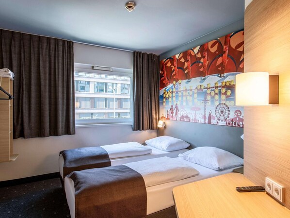 Habitación de hotel con dos camas, un escritorio, una lámpara y un ventanal con cortinas.
