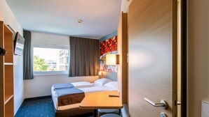 A hotel room with a bed, a desk, a chair, a TV, and a window. - B&B Hotel München City-west (Munich)