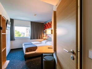 Ein Hotelzimmer mit Bett, Schreibtisch, Stuhl, Fernseher und Fenster.