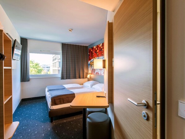A hotel room with a bed, a desk, a chair, a TV, and a window. - B&B Hotel München City-west (Munich)