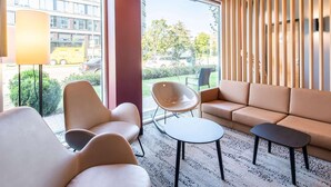 Un área de estar moderna con sofás de cuero, una mesa redonda y una silla. Amplios ventanales ofrecen vistas de la calle y edificios cercanos.