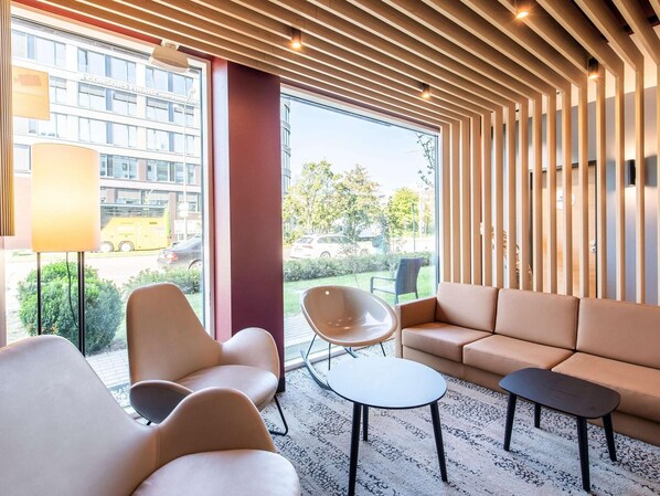 Ein moderner Loungebereich mit Ledersofas, einem runden Tisch und einem Sessel. Große Fenster bieten Blick auf die Straße und die umliegenden Gebäude.