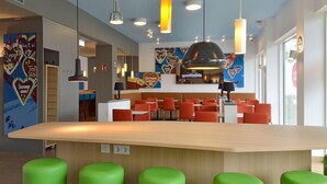 Een moderne bar met een houten toonbank, groene barkrukken en hanglampen.