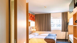 Habitación de hotel pequeña con una cama individual, un escritorio, una silla y una ventana con cortinas.
