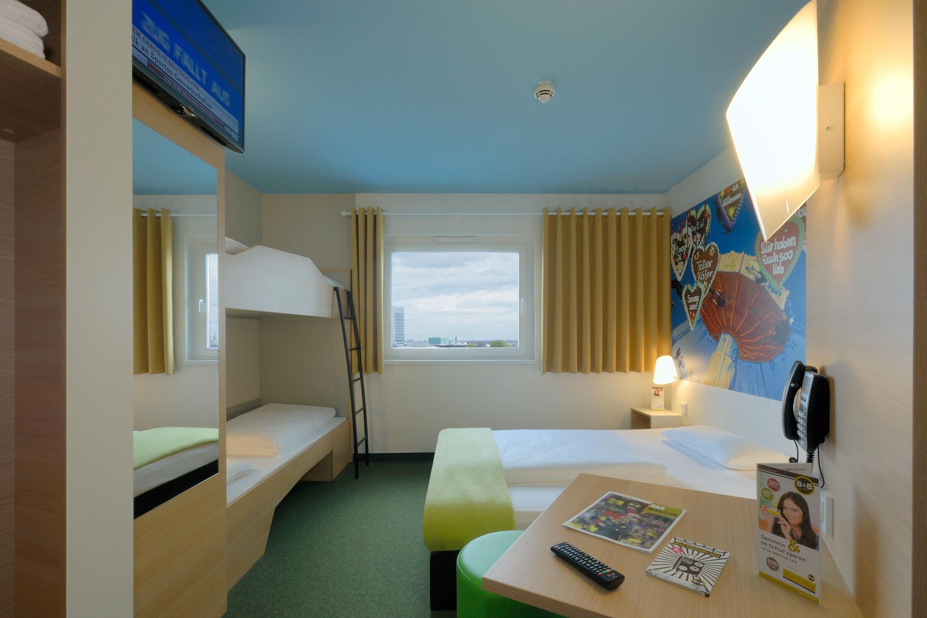 A hotel room with bunk beds, a desk with a remote control, a phone, and a poster on the wall.