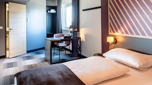 Una habitación de hotel con cama, escritorio con silla, mesita y ventana con cortinas.