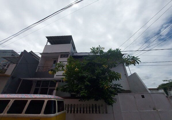 A building with a white facade, a balcony, and a tree with yellow flowers. - Eiffel Residence Cideng by Zuzu (Jakarta)