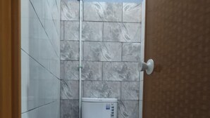 Ein Badezimmer mit Toilette, gefliesten Wänden und einer Duschkabine.