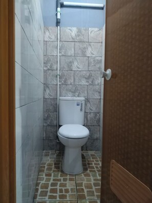 A bathroom with a toilet, tiled walls, and a shower area. - Eiffel Residence Cideng by Zuzu (Jakarta)